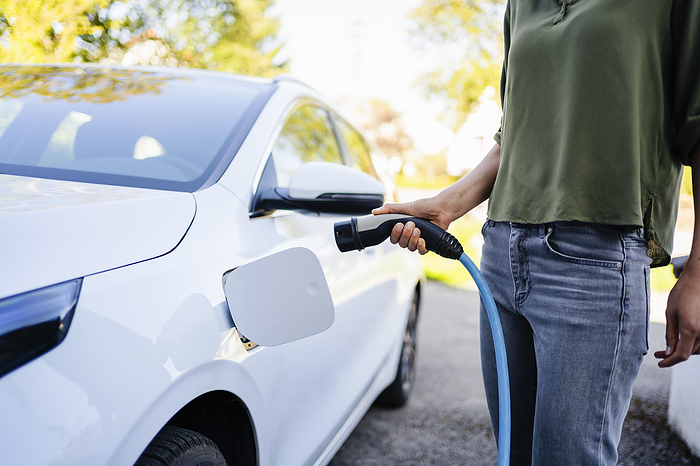Woman holding plug near electric car at charging station