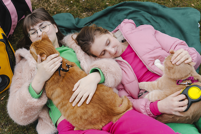 Smiling young women lying with cats on blanket