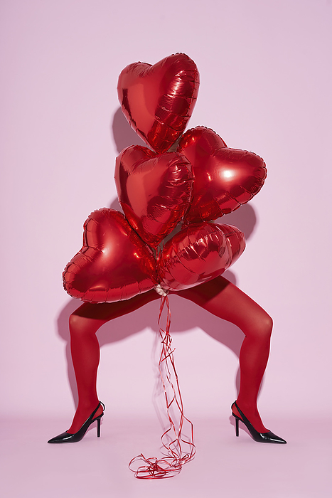 A woman stands on a pink background in red tights Women wearing stocking holding red balloons