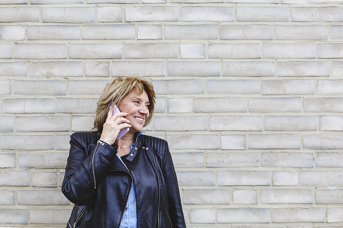Senior woman talking on smart phone in front of brick wall