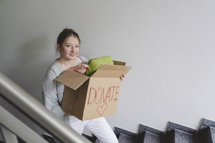 Teenage girl with clothes in box for donation moving up on steps