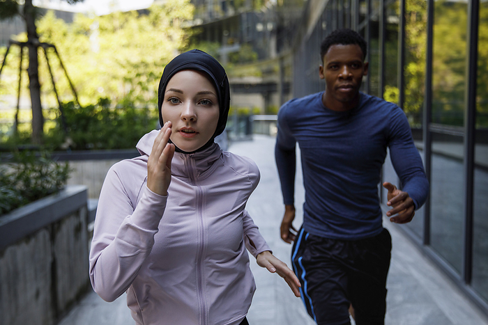 Determined woman wearing hijab running with friend on footpath