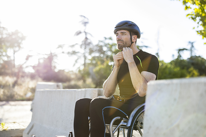 Mature athlete fastening sports helmet sitting on wheelchair