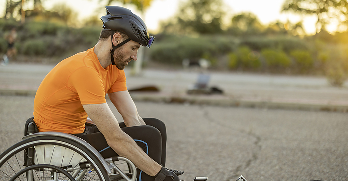 Sportsman with helmet sitting in wheelchair on road