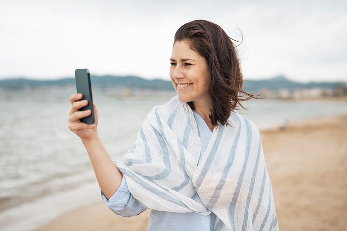 Smiling woman taking selfie through smart phone at beach