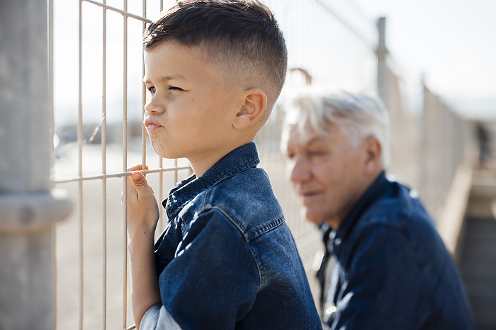 Curious boy puckering and looking through fence by grandfather