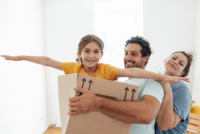 Happy woman with man carrying daughter in cardboard box and having fun at home