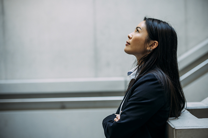 Businesswoman looking up with arms crossed leaning on railing at workplace