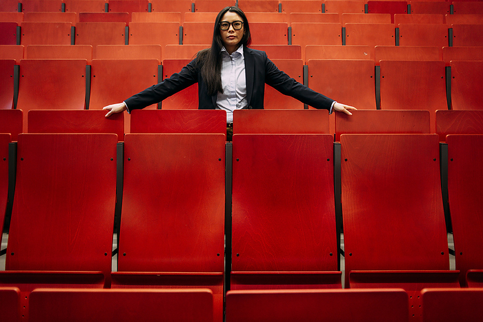 Confident businesswoman amidst red seats in convention center