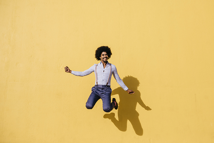 Josep Maria Rovirosa Smiling man jumping in the air in front of yellow wall