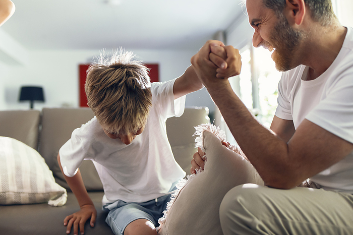 Happy father holding son's hand sitting on sofa