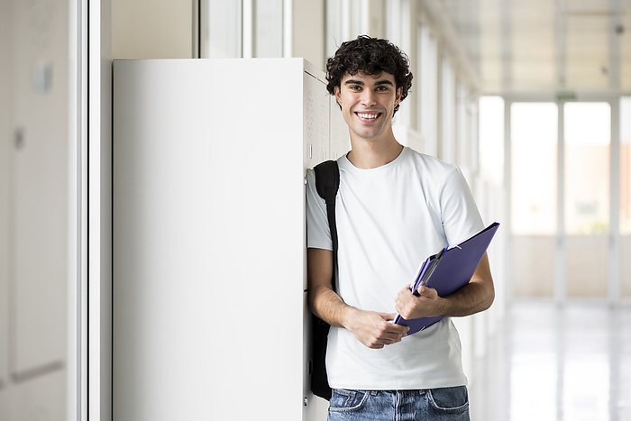 Smiling student holding file folder in corridor