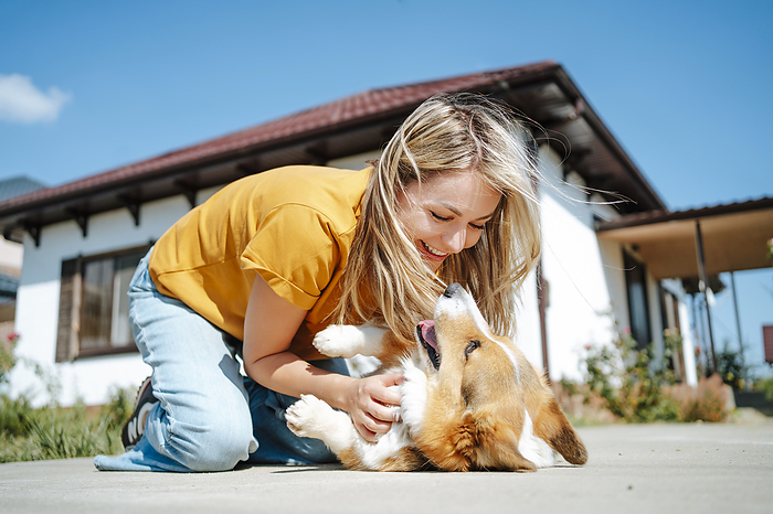 Happy woman playing with corgi dog in front of house on sunny day
