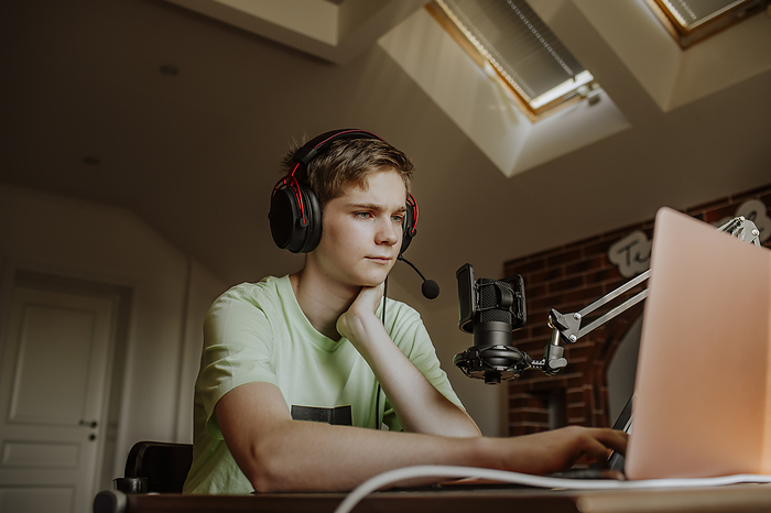 Teenage boy podcasting in front of laptop at home