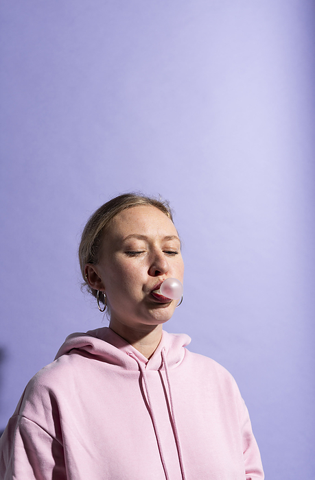 Studio Line Woman blowing bubble gum against purple background