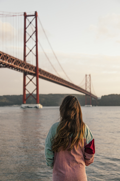 Young woman visiting Lisbon Young woman admiring Tagus river with April 25th Bridge at sunset