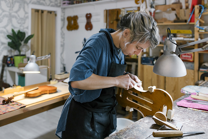Young luthier working at her workshop Luthier carving on violin at desk in workshop