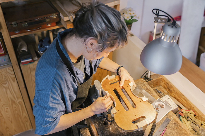 Young luthier working at her workshop Luthier making parts of violin on desk in workshop