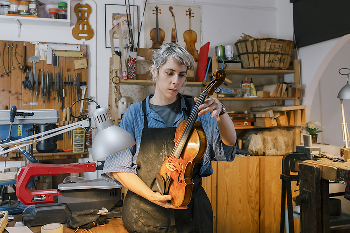 Young luthier working at her workshop Luthier examining violin in workshop