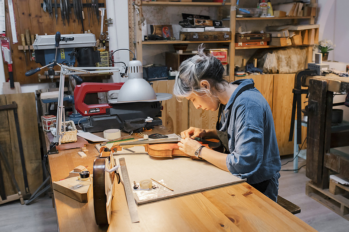 Young luthier working at her workshop Female craftsperson working on violin at desk in workshop