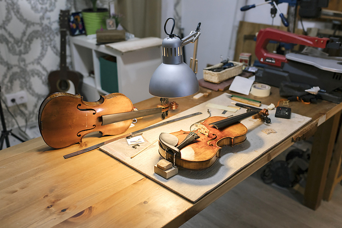 Young luthier working at her workshop Unfinished violins kept under desk lamp in workshop