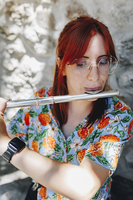 Redhead woman wearing eyeglasses practicing flute