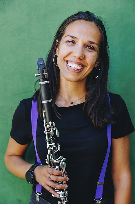 Happy woman holding clarinet in front of wall