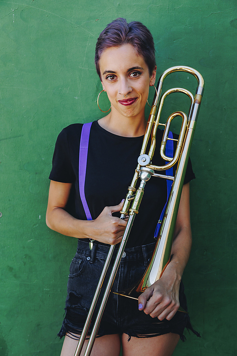 Smiling woman holding trombone in front of wall