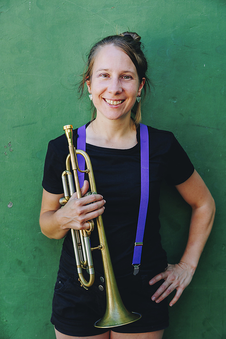 Smiling woman with hand on hip holding trumpet in front of wall