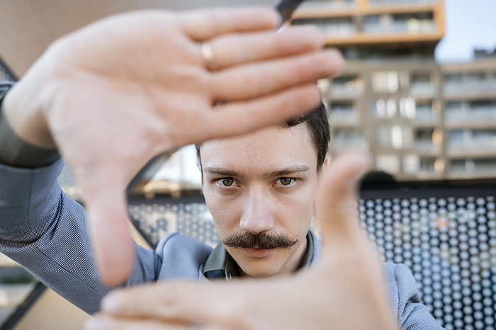 Confident businessman with mustache making finger frame in front of office building
