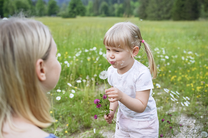 Daughter blowing dandelion looking at mother