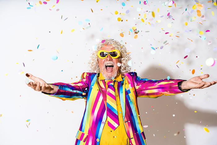 Cheerful man enjoying with confetti against white background