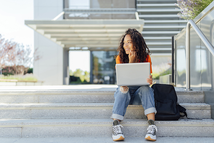 Smiling student sitting with laptop on steps in campus