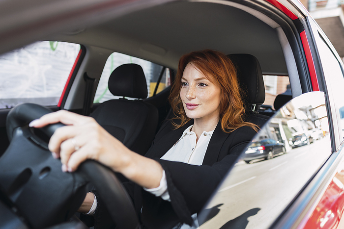 Smiling redhead businesswoman driving car