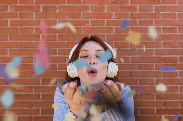 Woman wearing wireless headphones blowing confetti
