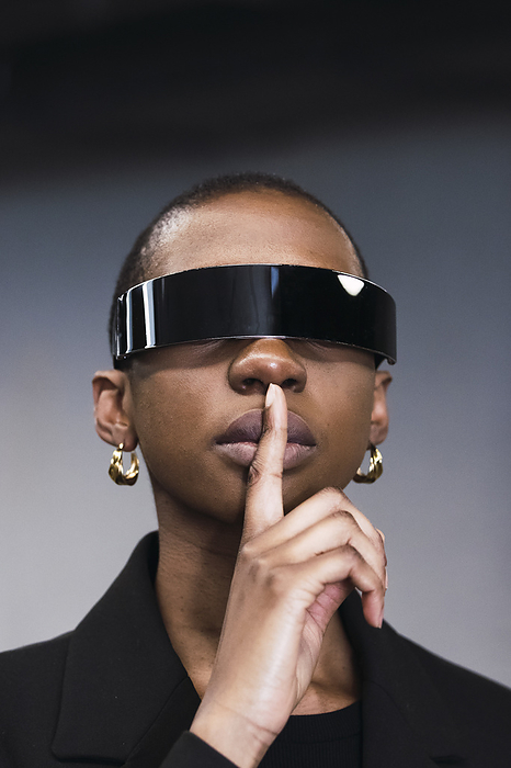 Young woman with finger on lips and wearing smart glasses