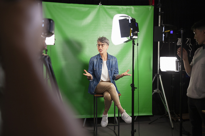 Mid adult woman giving an interview while sitting against green screen