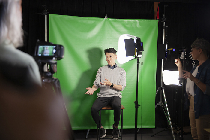 Young adult man giving an interview while sitting against green screen