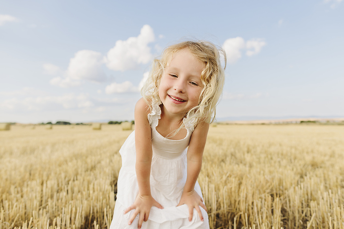 Happy blond girl standing in stubble field with hands on knees