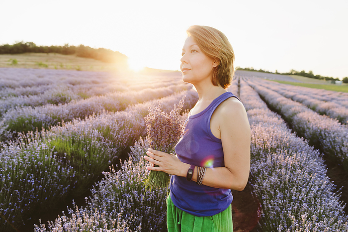 Thoughtful woman holding bouquet of lavender flowers in field