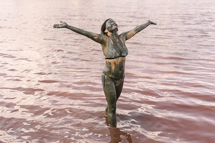 Smiling woman with arms outstretched standing in lake