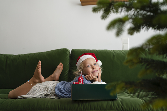 Smiling girl lying on sofa with box of Christmas decorations