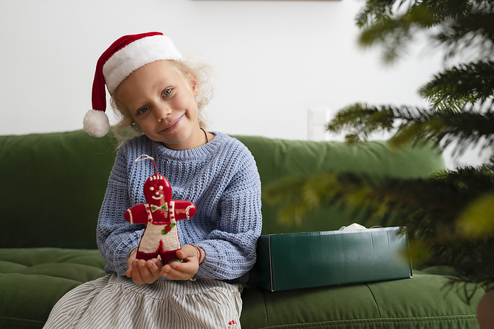 Smiling girl holding Christmas decoration on sofa at home