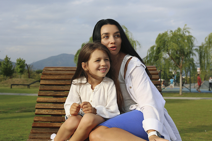 Smiling girl sitting with mother on lounge chair in park