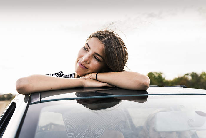 Smiling young woman looking out of sunroof of a car