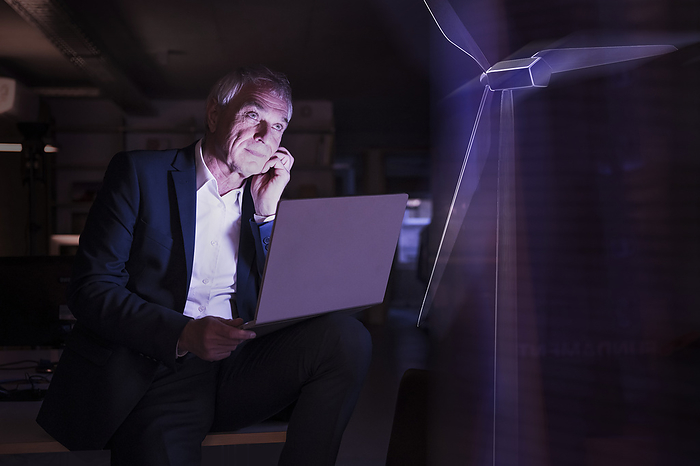 Businessman with laptop looking at futuristic wind turbine in office