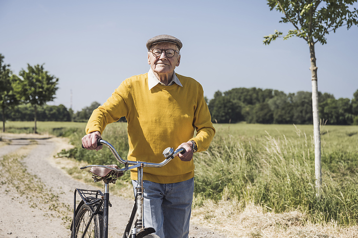 Smiling senior man walking with bicycle on sunny day