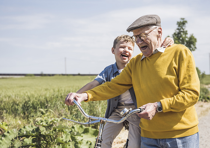 Cheerful senior man with grandson sitting on bicycle