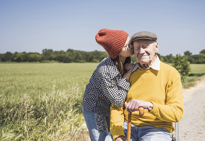 Girl wearing knit hat kissing grandfather on sunny day