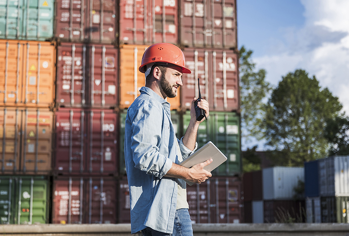 Foreperson wearing hardhat talking on walkie-talkie in front of containers